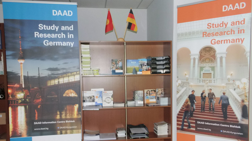 A shelf with brochures flanked by roll-ups with DAAD lettering.